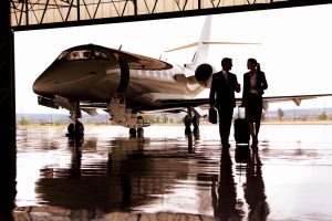 Business professionals walking towards a parked private jet in a hangar, suited for an ultra-high-net-worth lifestyle.