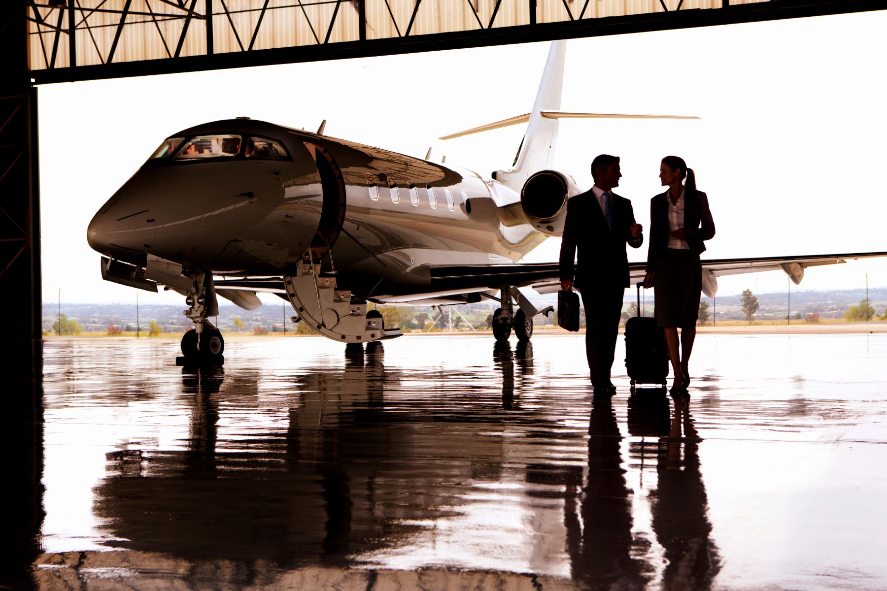 Business professionals walking towards a parked private jet in a hangar, suited for an ultra-high-net-worth lifestyle.