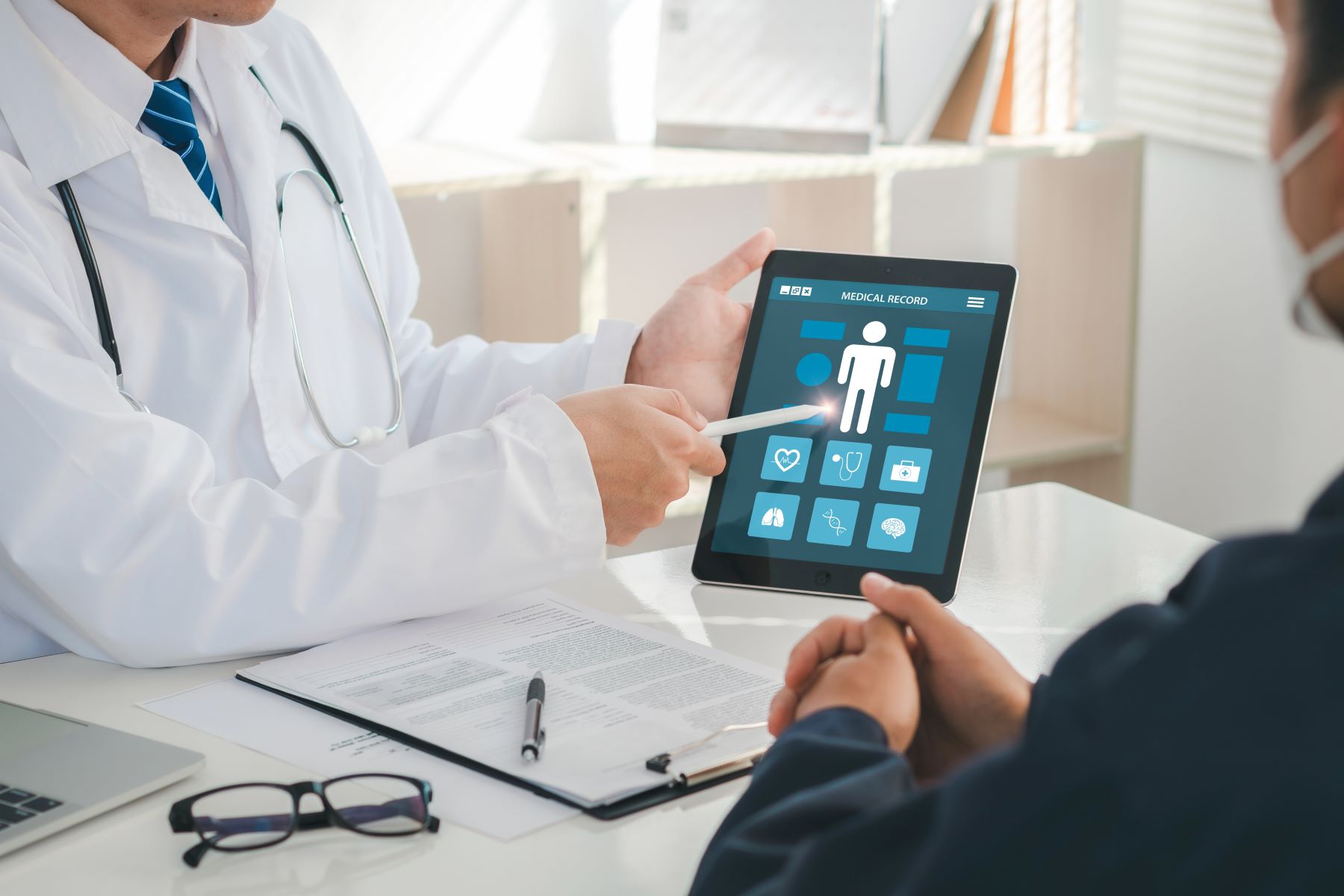 A healthcare professional discusses medical records on a tablet with a patient during a health screening appointment.