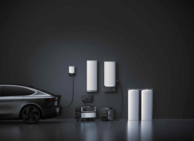 A black vehicle is parked beside white energy storage units and smart devices on a dark wall, showcasing energy sovereignty technology.