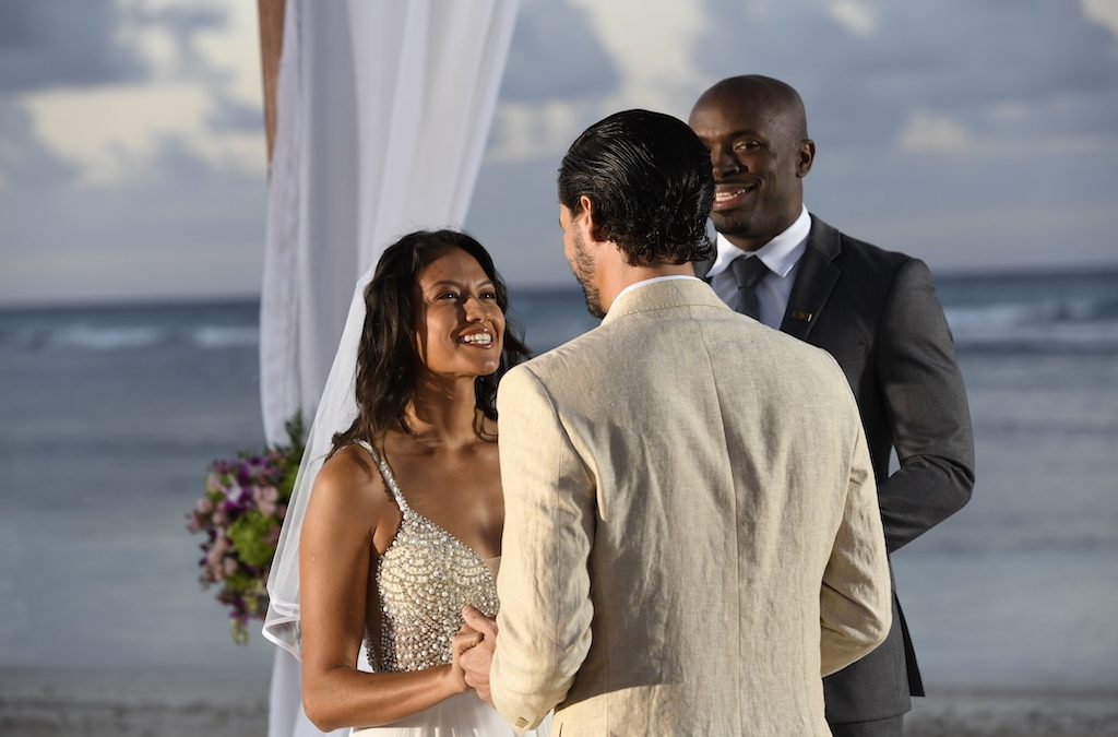 A couple exchanges vows on a beach during their wedding ceremony, with a celebrant and ocean backdrop.
