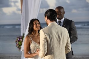 A couple exchanges vows on a beach during their wedding ceremony, with a celebrant and ocean backdrop.