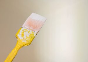 Paintbrush with yellow handle against a soft beige background, ideal for high-end home remodeling projects.