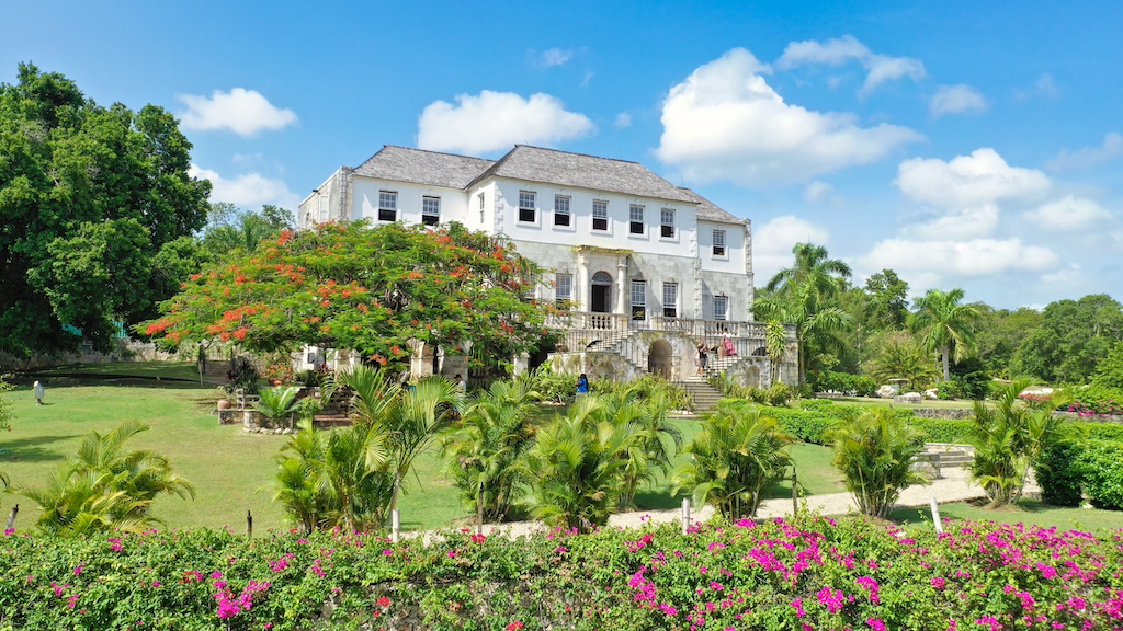 Historic estate surrounded by lush greenery and vibrant flowers, showcasing a bright blue sky ideal for a Jamaican wedding.