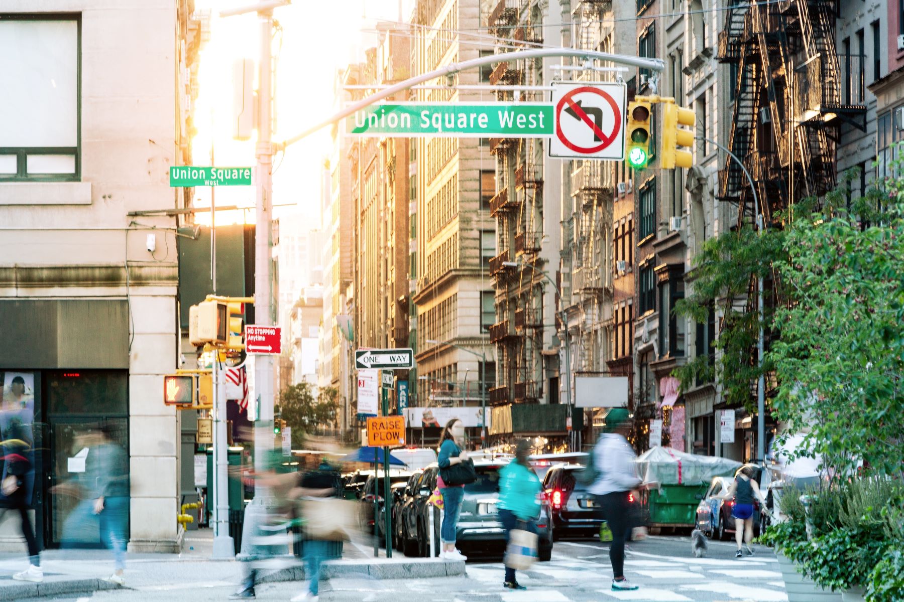 Crowded street scene at Union Square in NYC with pedestrians, traffic, and city buildings in warm evening light.