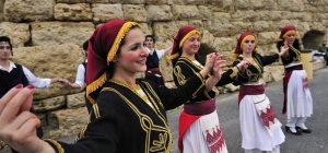 Traditional Cretan dancers perform in traditional attire, showcasing the vibrant culture of Crete against a stone backdrop.