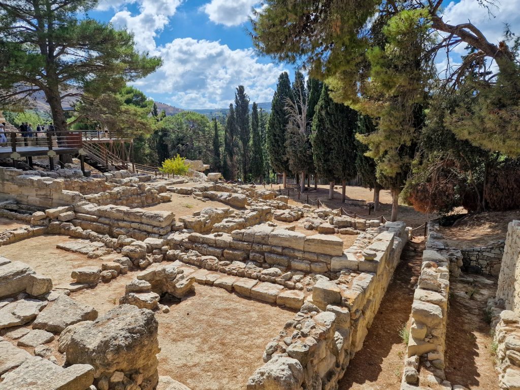 Ancient ruins set amidst trees under a partly cloudy sky, showcasing Crete's historical landscape and natural beauty.