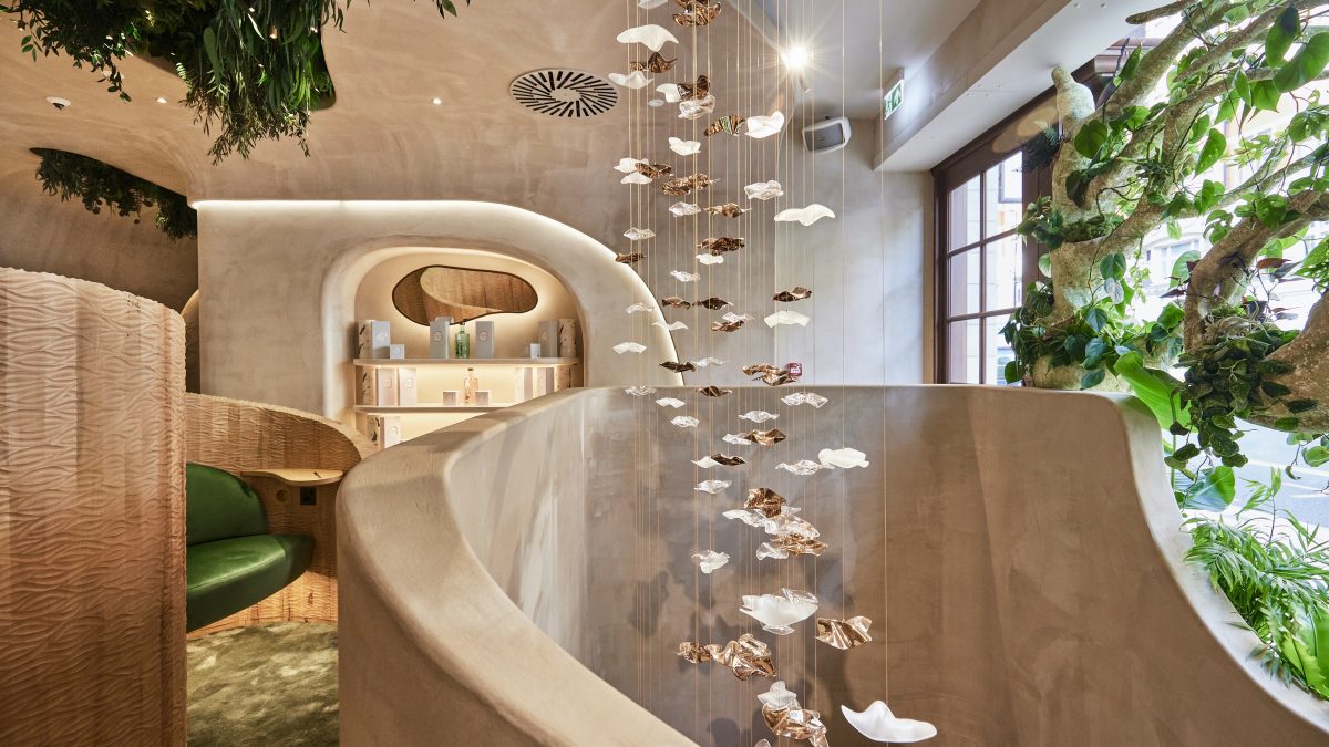 Interior of a holistic beauty space featuring hanging art pieces, lush greenery, and a modern, curved design aesthetic.