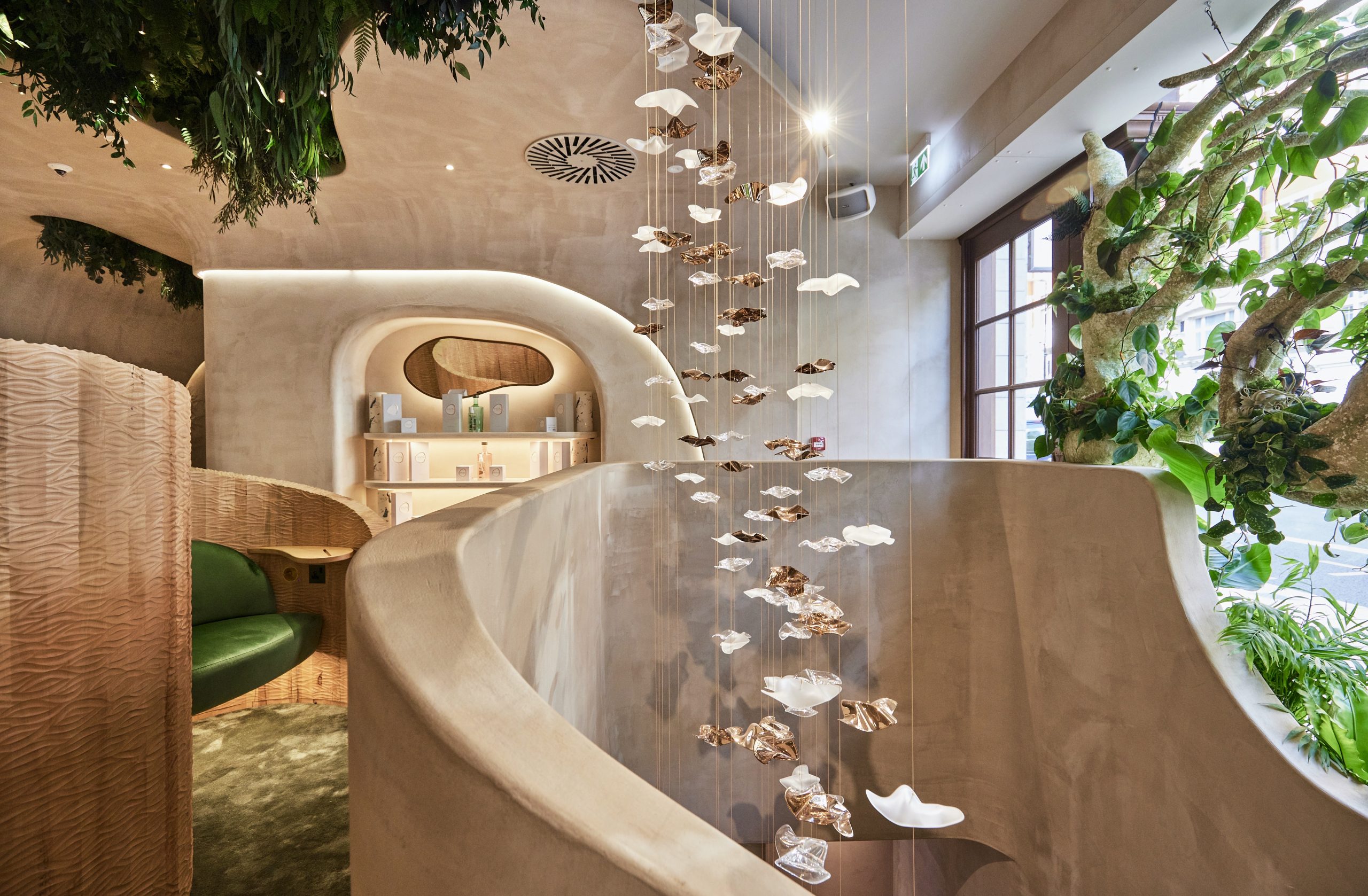 Interior of a holistic beauty space featuring hanging art pieces, lush greenery, and a modern, curved design aesthetic.