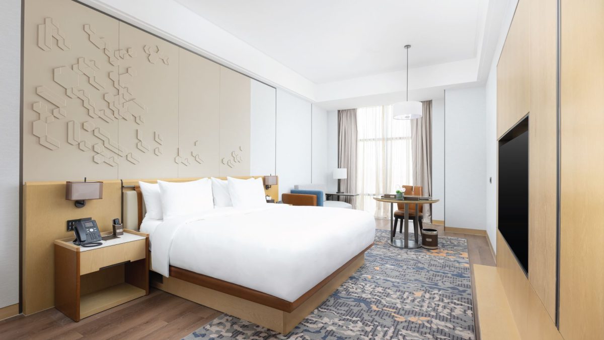 Modern hotel room featuring a king-sized bed, stylish decor, a cozy seating area, and large windows with natural light.