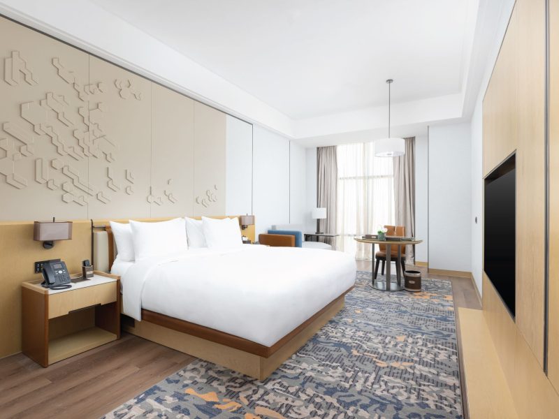 Modern hotel room featuring a king-sized bed, stylish decor, a cozy seating area, and large windows with natural light.