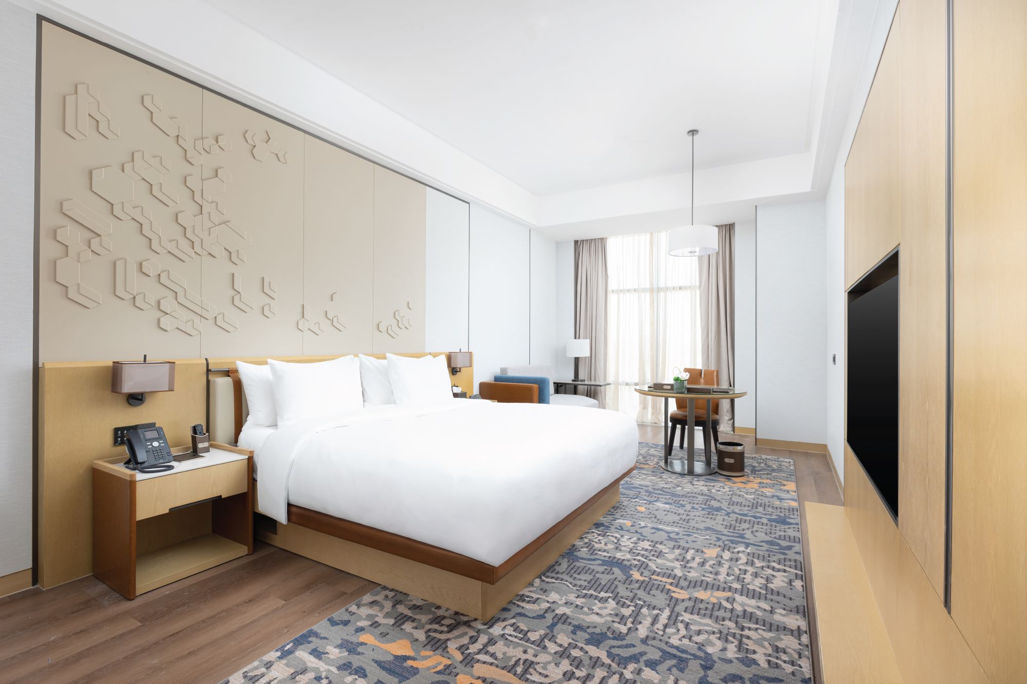 Modern hotel room featuring a king-sized bed, stylish decor, a cozy seating area, and large windows with natural light.