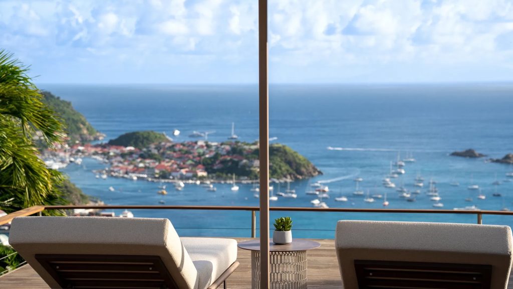 Luxury villa view overlooking the vibrant harbor and lush hills of St. Barthélemy, featuring lounge chairs and a modern setting.