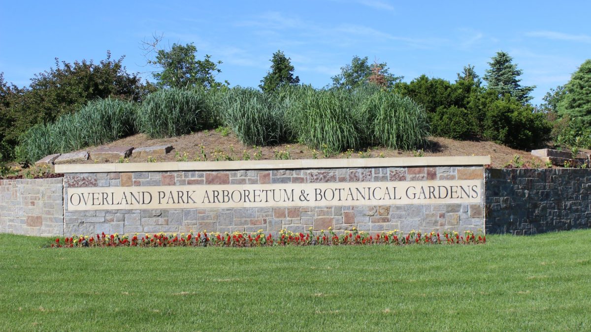 Signage for Overland Park Arboretum and Botanical Gardens, surrounded by greenery and colorful flowers.