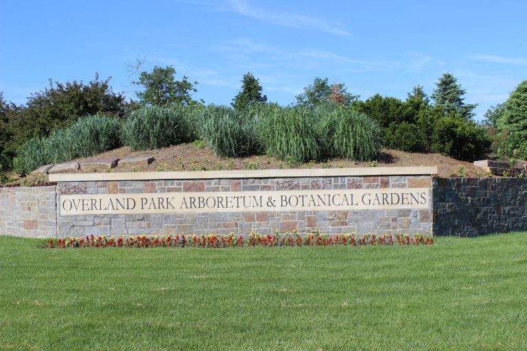 Signage for Overland Park Arboretum and Botanical Gardens, surrounded by greenery and colorful flowers.