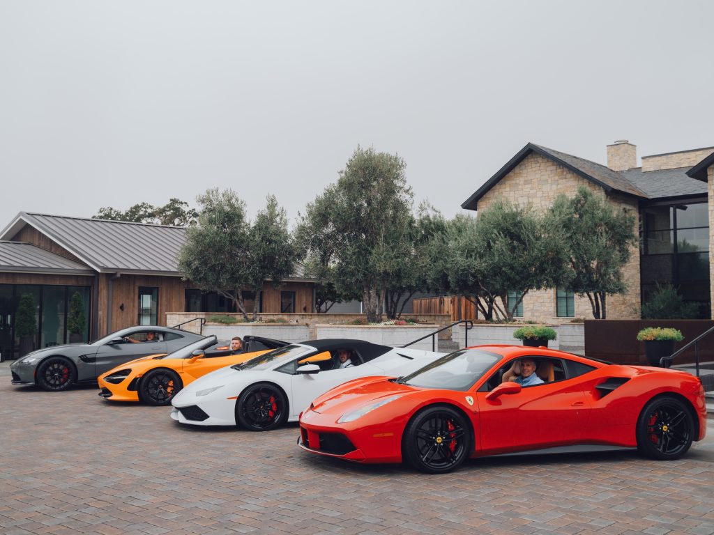 Luxury sports cars in various colors parked outside Four Seasons Resort Napa Valley, with people inside some of the vehicles.