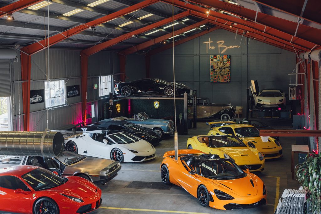 A collection of luxury sports cars displayed in a vibrant garage, showcasing brands like Ferrari, Lamborghini, and McLaren.