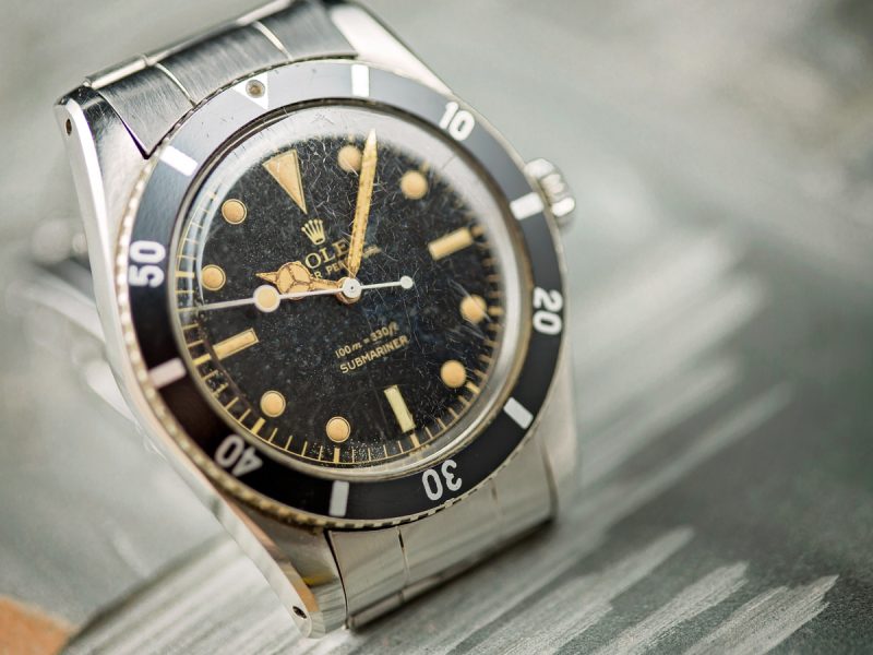 Vintage Rolex Submariner watch with a black dial and gold markers, showcasing its iconic design and aged patina.