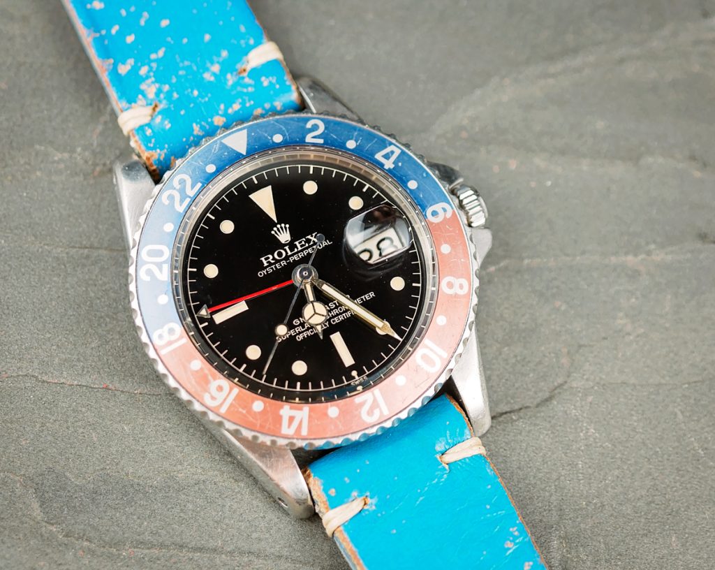Vintage Rolex watch with a black dial and blue bezel, featuring a blue leather strap, showcased for collectors at Bob's Watches.