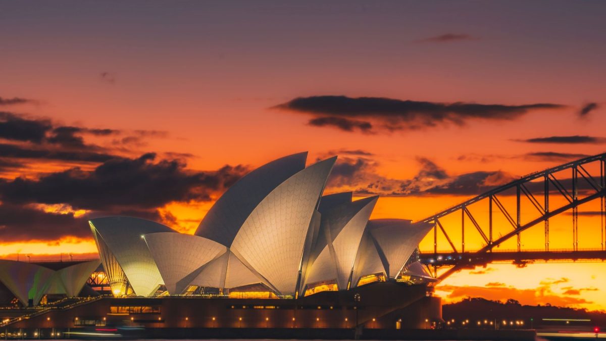 Sydney Opera House illuminated at sunset with the Sydney Harbour Bridge in the background.