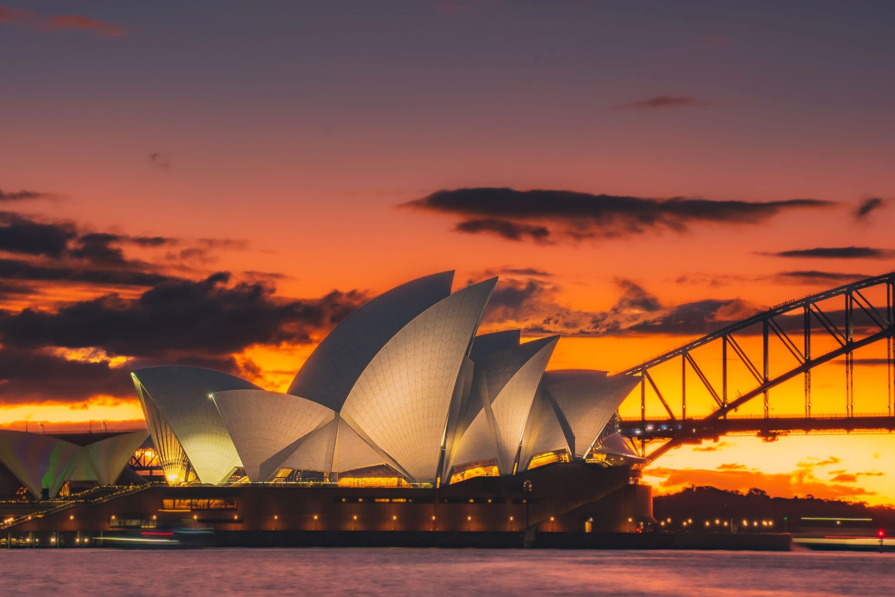 Sydney Opera House illuminated at sunset with the Sydney Harbour Bridge in the background.