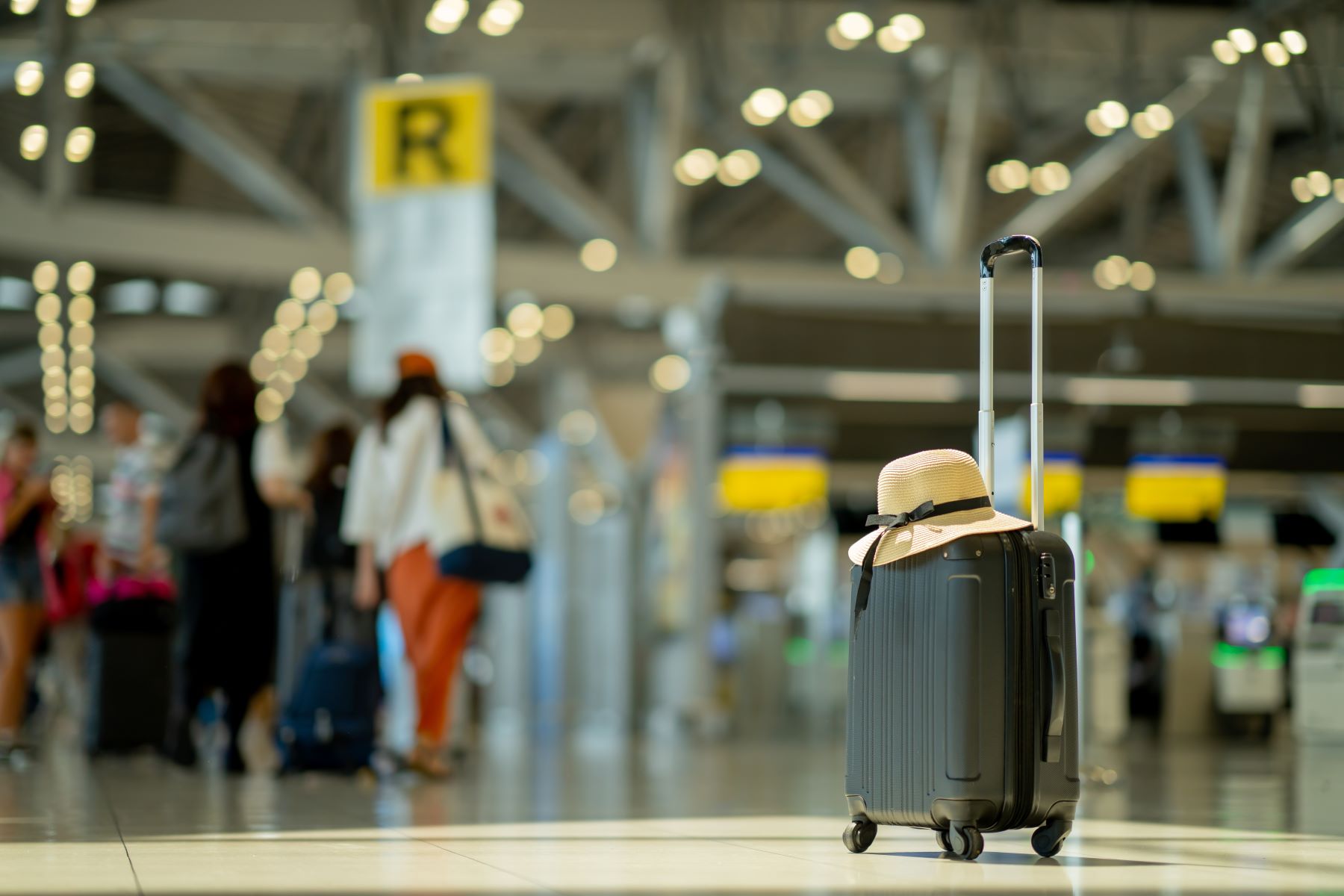 A suitcase with a sun hat sits on the floor of a busy airport terminal.