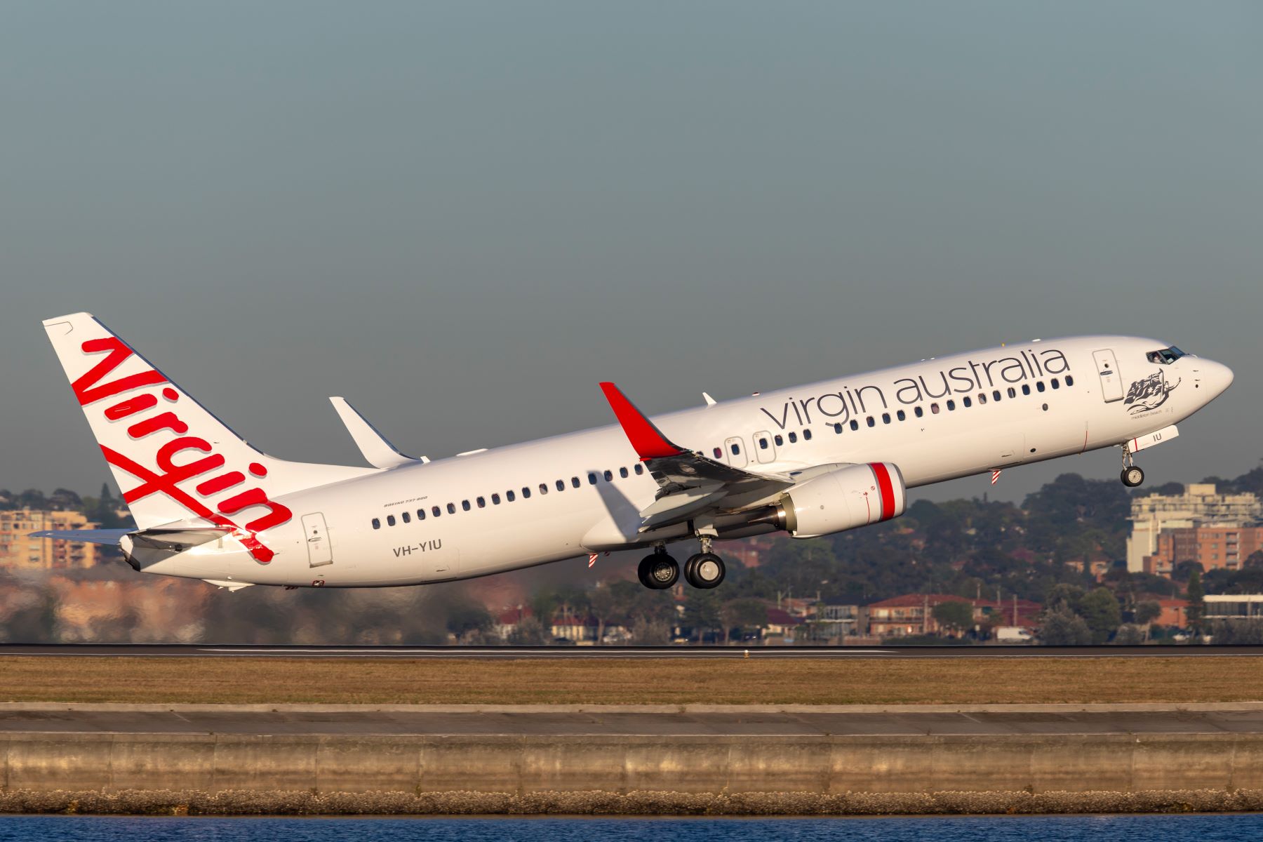 Virgin Australia airplane taking off, showcasing its distinctive livery against a clear, sunny sky.