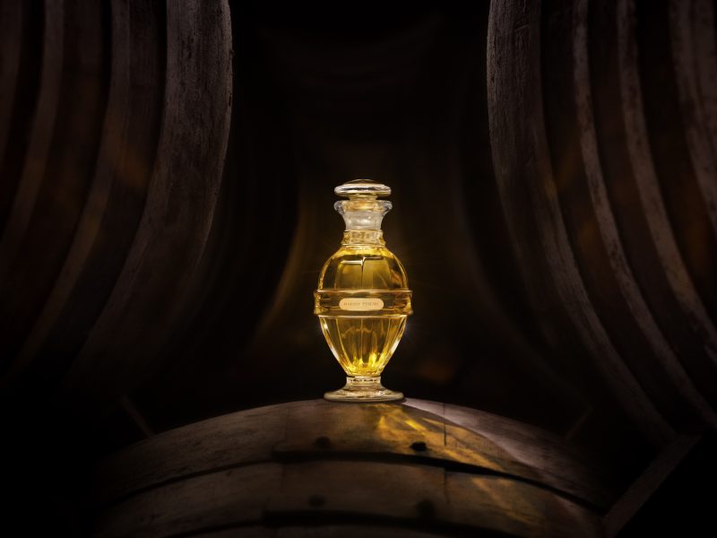 Elegant glass perfume bottle glowing amidst dark wooden barrels, representing the essence of Maison Psyché's luxurious fragrance.