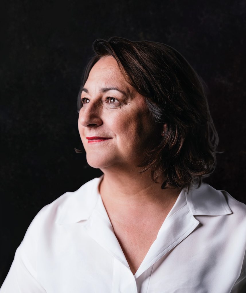 Profile shot of a woman in a white blouse against a dark background, exuding confidence and elegance.