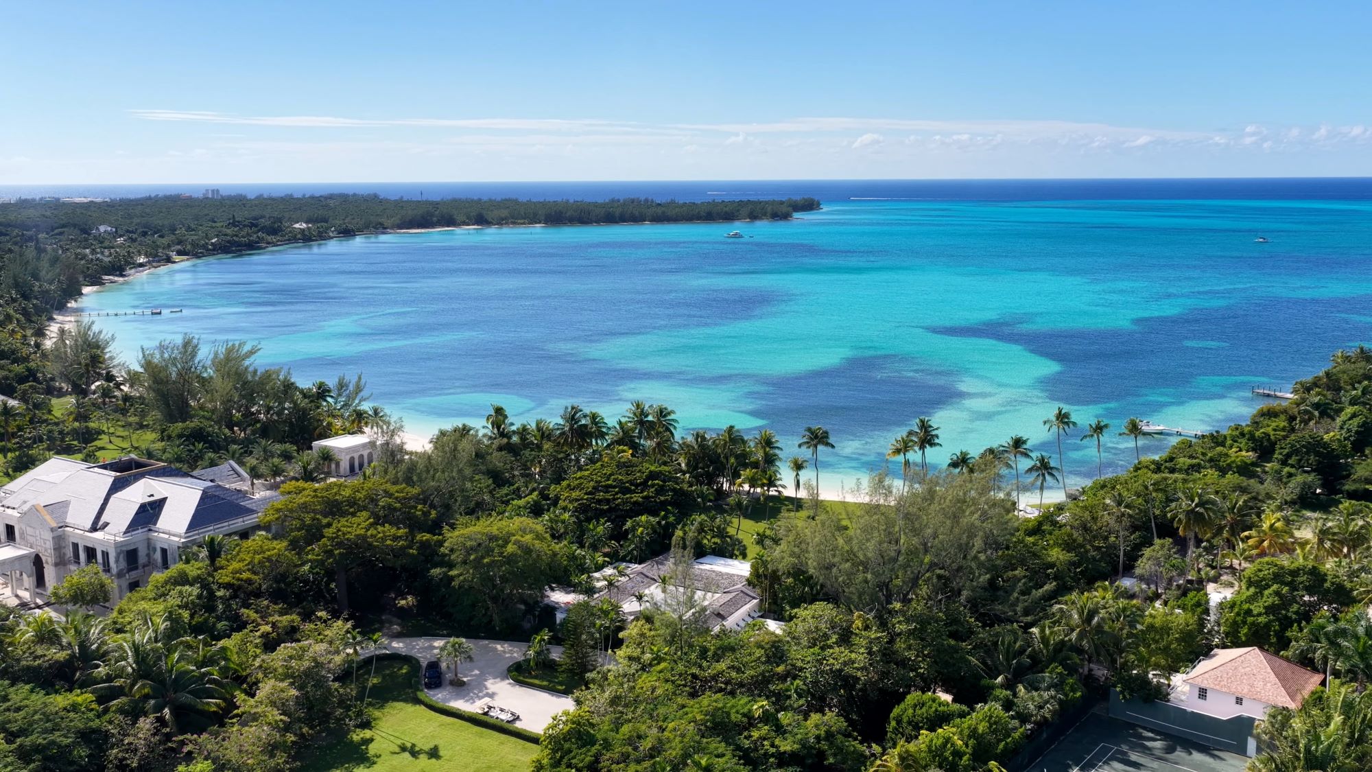 Aerial view of turquoise waters and sandy beaches surrounded by lush greenery and luxury homes in the Bahamas.