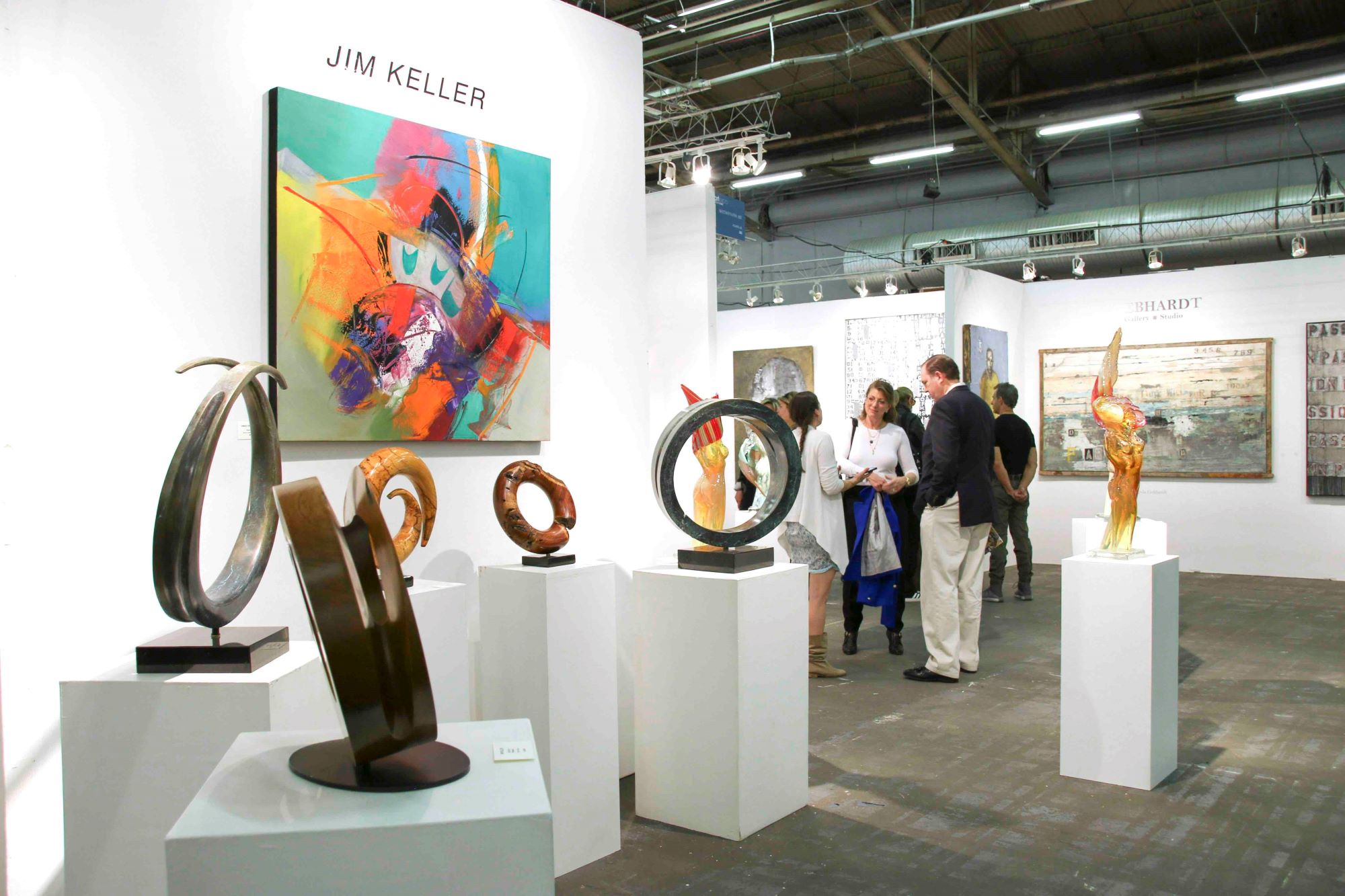 Sculptures and an abstract painting by Jim Keller displayed at Artexpo New York, with visitors engaging in conversation.