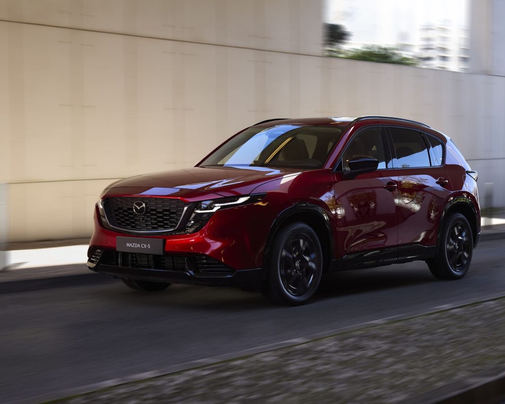 2026 Mazda CX-5 in red driving through a modern urban setting.