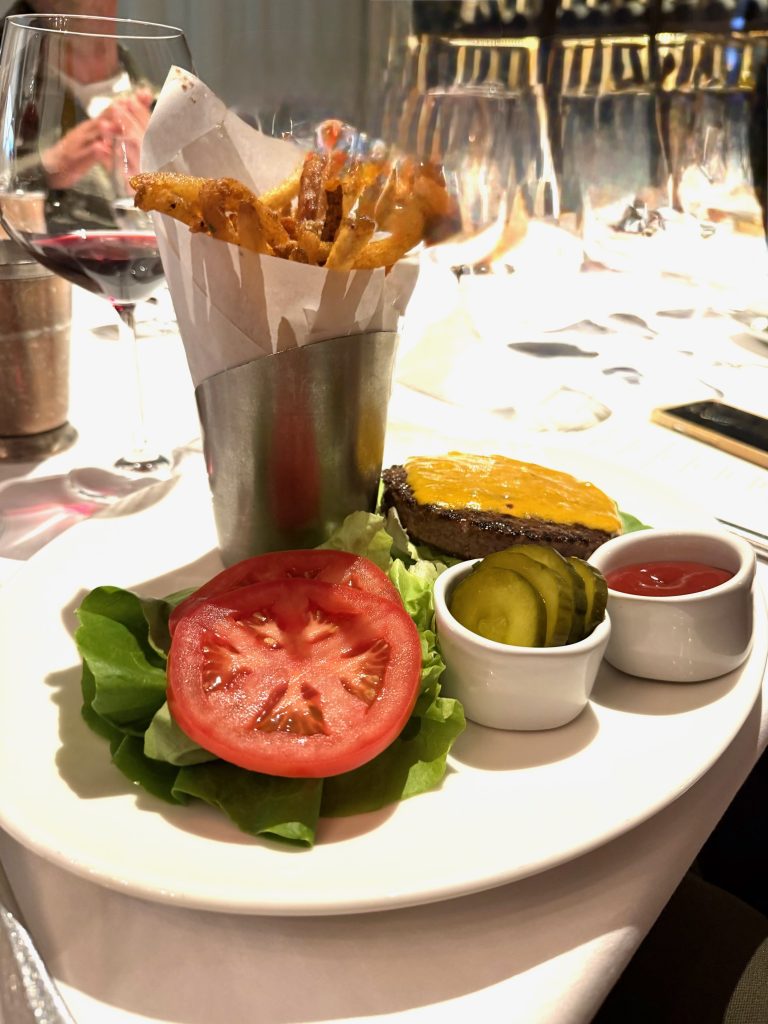 A gourmet cheeseburger with lettuce, tomato, pickles, and ketchup accompanied by a side of crispy fries.