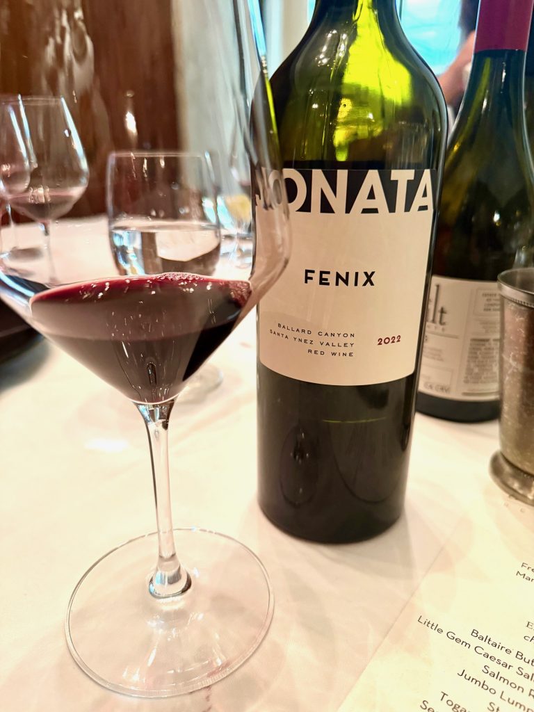 A glass of red wine beside a bottle of Sonata Fenix, with a restaurant menu partially visible in the background.