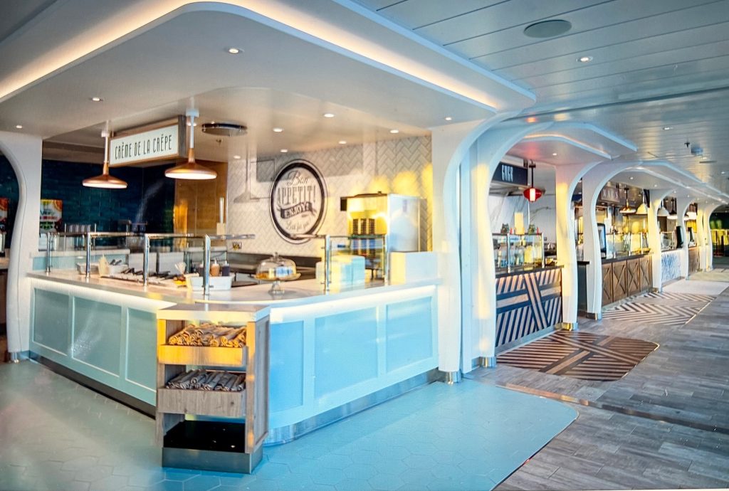 Modern dining area featuring a crepe station with illuminated signage and a variety of food service counters onboard.