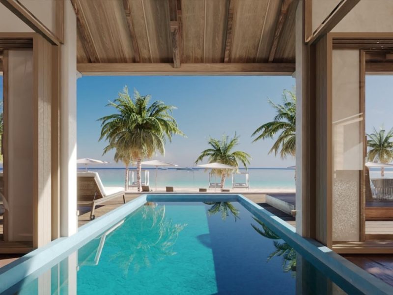 View of a serene pool area with tropical plants and umbrellas, leading to a tranquil beach and ocean in the background.