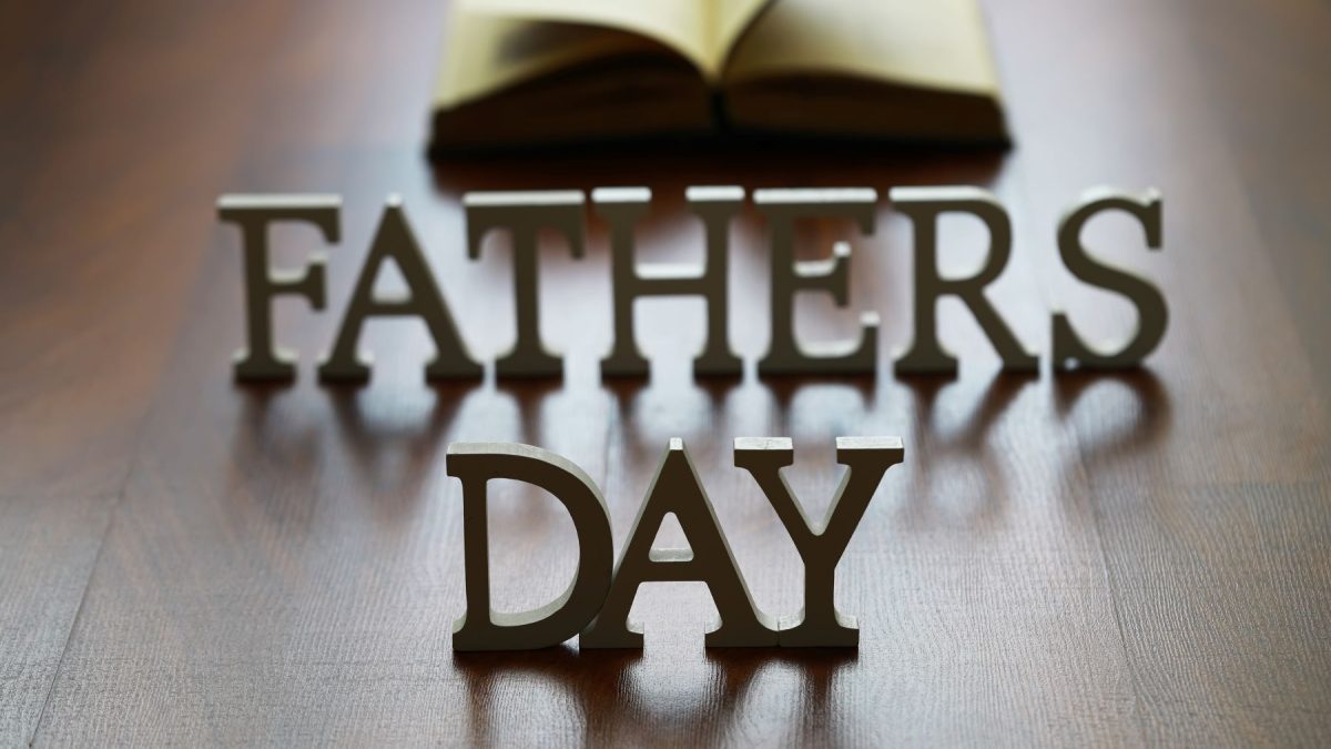 "Decorative letters spelling 'Father's Day' with an open book in the background on a wooden surface."