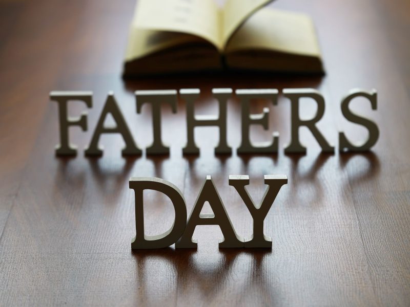 "Decorative letters spelling 'Father's Day' with an open book in the background on a wooden surface."