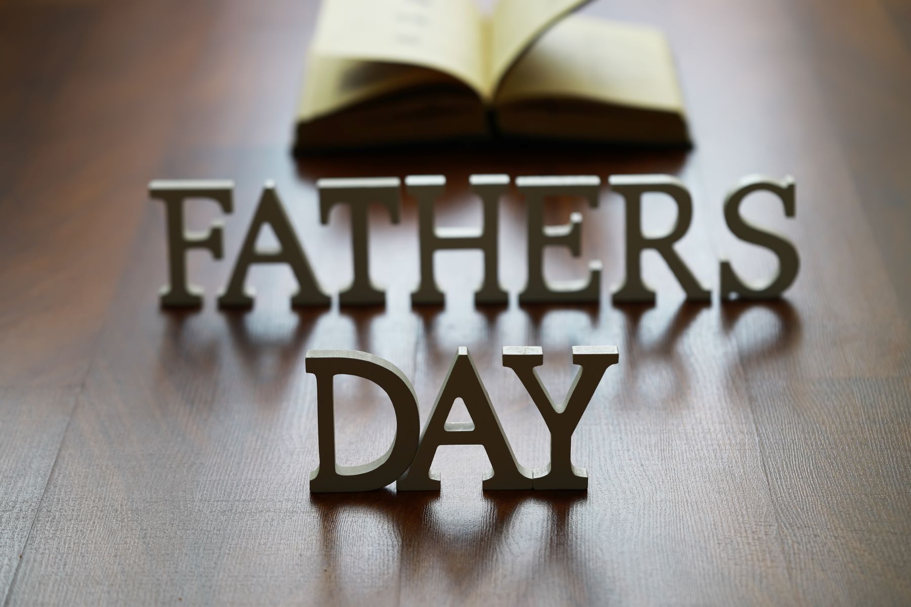 "Decorative letters spelling 'Father's Day' with an open book in the background on a wooden surface."