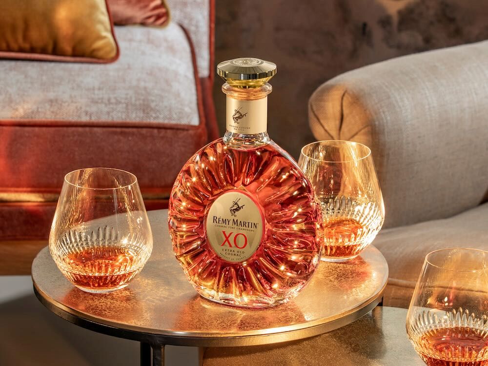 Rémy Martin XO bottle sits on a table surrounded by two tumblers filled with cognac, set in a stylish living room.