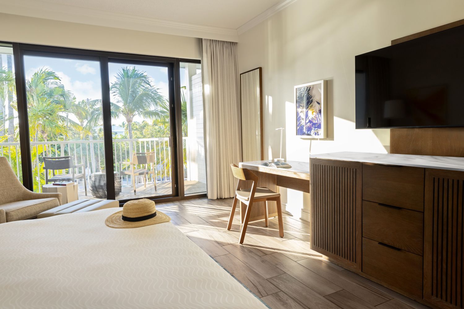 Bright and airy guestroom at Hawks Cay Resort featuring a king bed, work desk, and large windows overlooking palm trees.