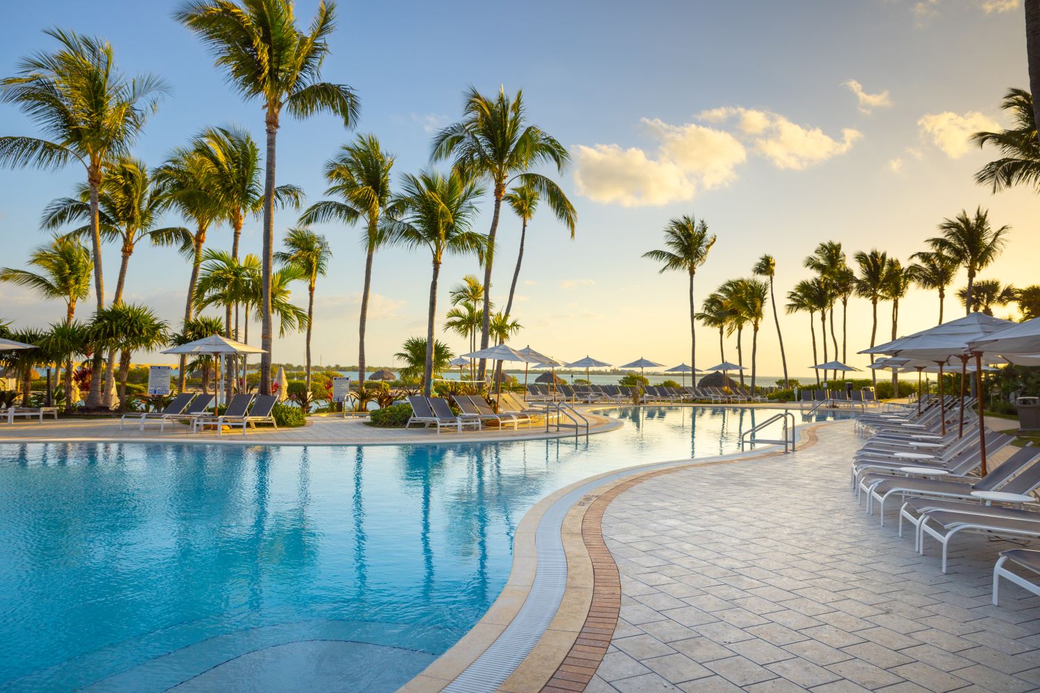 A serene poolside view at Hawks Cay Resort, surrounded by palm trees and lounge chairs under a beautiful sunset sky.