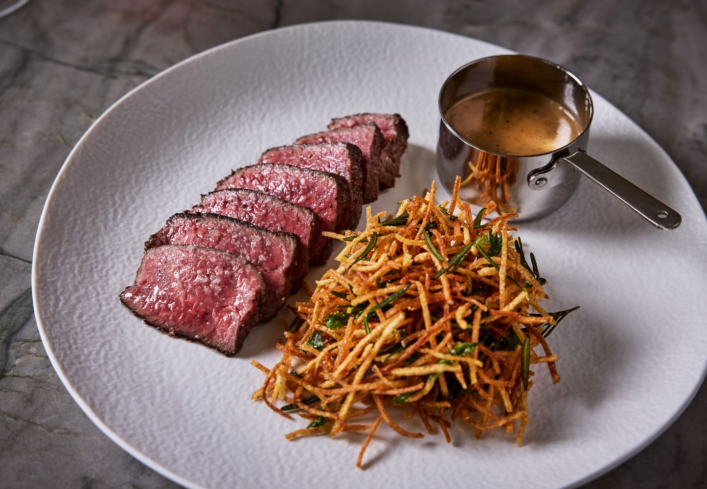 Tender steak frites with crispy shoestring potatoes and a rich sauce, served on a white plate.