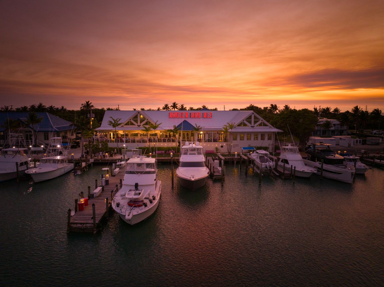 Angler and Ale restaurant at dusk, surrounded by boats in a marina under a colorful sunset sky.