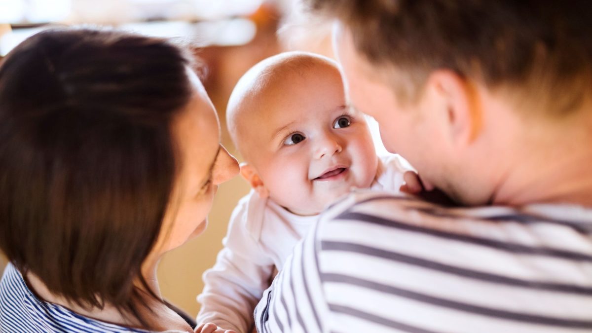 Smiling baby being held by parents, capturing a joyful moment in family life.