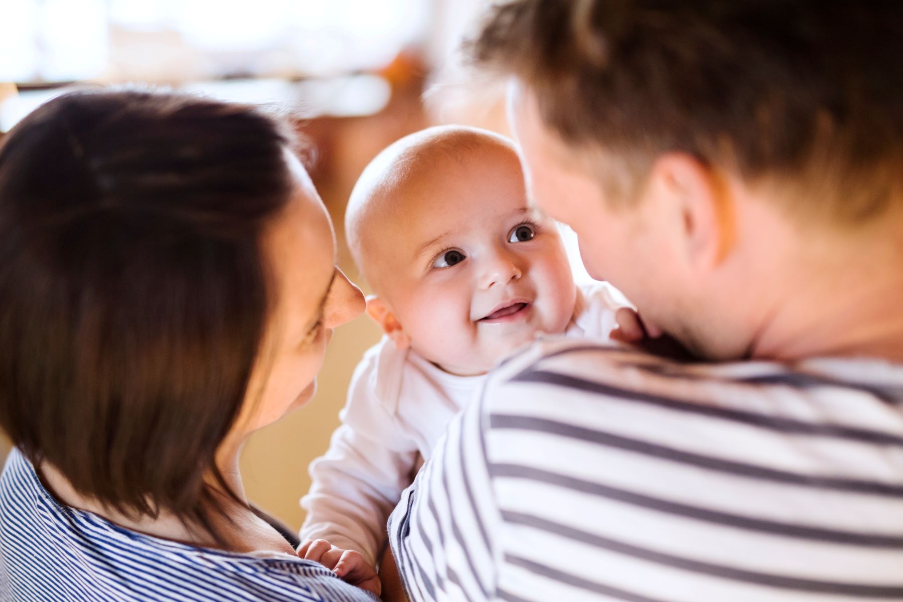 Smiling baby being held by parents, capturing a joyful moment in family life.