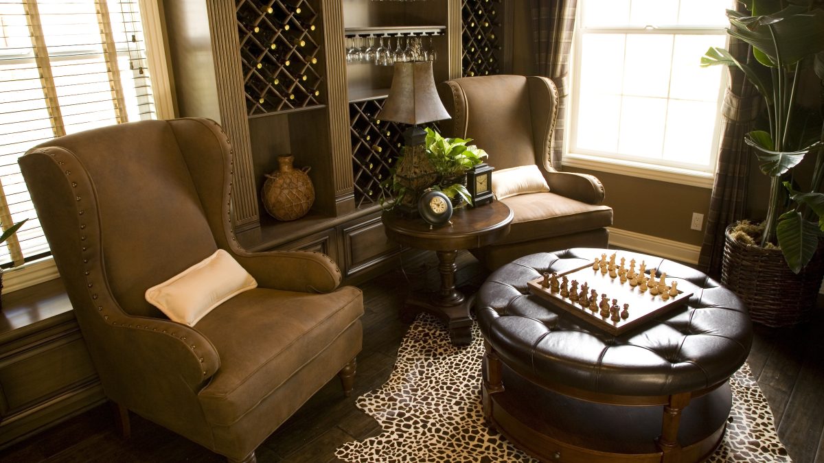 Luxurious cigar lounge featuring leather chairs, a chess set on a table, and elegant decor with a wine rack and plant.