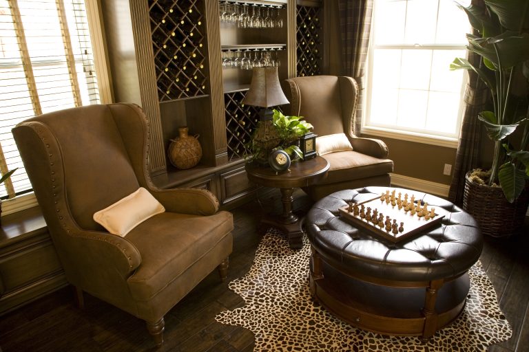 Luxurious cigar lounge featuring leather chairs, a chess set on a table, and elegant decor with a wine rack and plant.