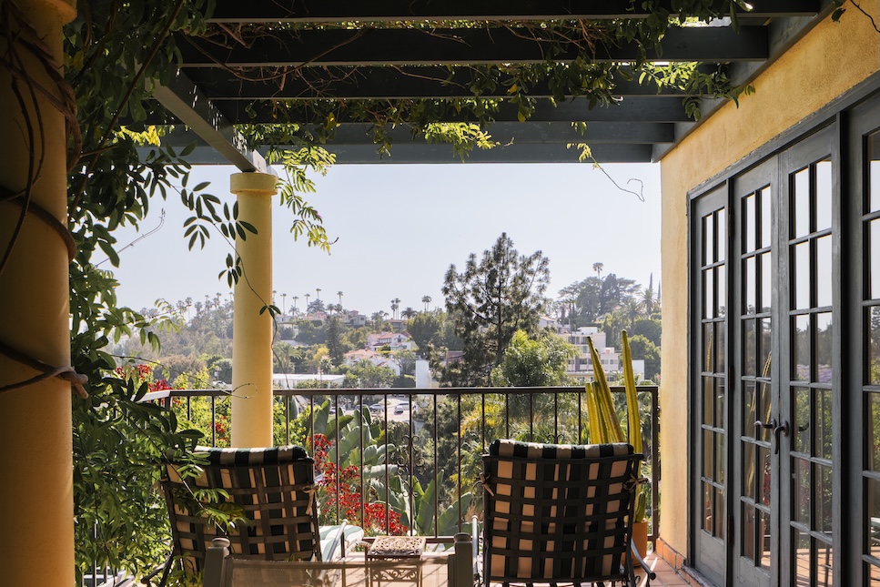 Balcony view of Casa Ivarene, featuring lush greenery and a glimpse of the Hollywood Hills in the background.