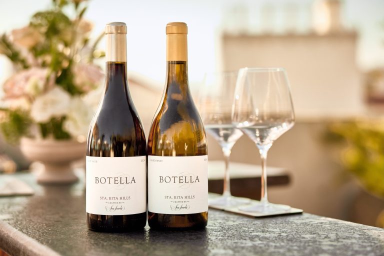Two bottles of Sea Smoke Botella wine with glasses in the background, set on a dark stone surface.